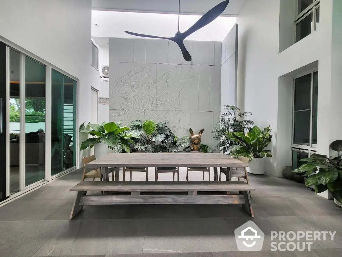 Spacious modern living area with high ceiling, large fan, and lush indoor plants creating a tranquil urban oasis.