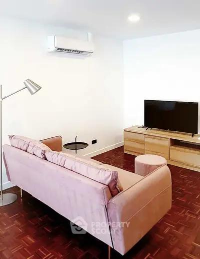 Modern living room with pink sofa, TV, and stylish floor lamp on wooden flooring.