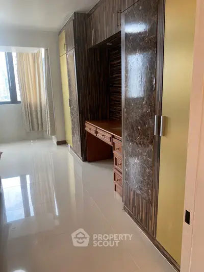 Spacious bedroom with built-in wooden wardrobe and glossy floor tiles