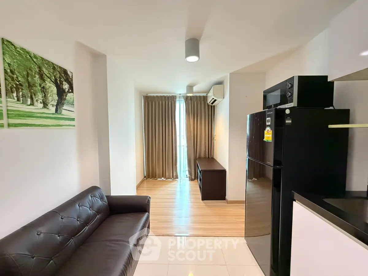 Modern living room with sleek black sofa and stainless steel fridge, featuring elegant wooden flooring and natural light.