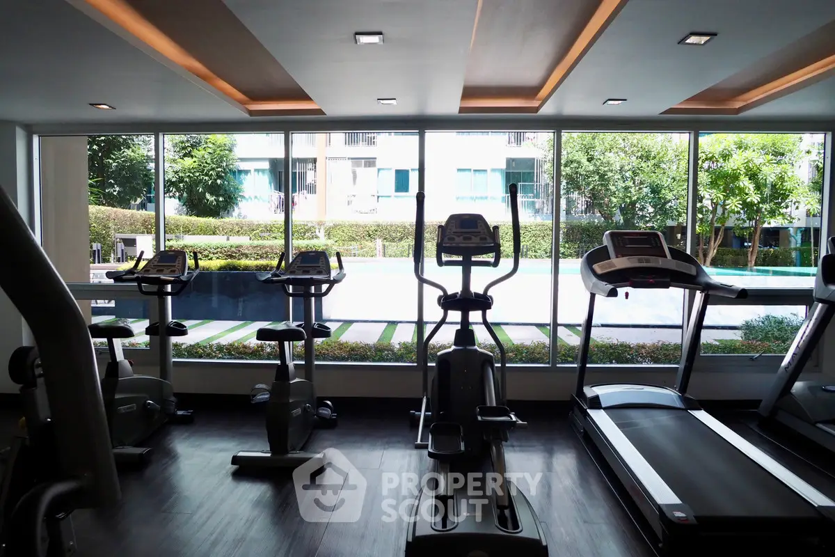 Modern gym with exercise equipment and large windows overlooking greenery.