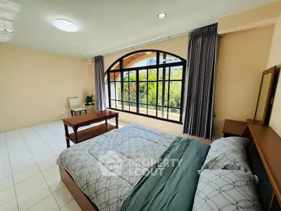 Spacious bedroom with large window and garden view, featuring elegant furnishings and natural light.