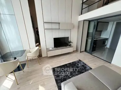 Modern living room with high ceiling and mezzanine, featuring sleek furniture and open kitchen view.