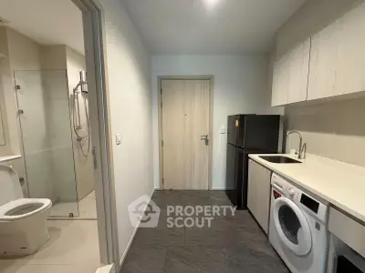Modern apartment entry with compact kitchen and bathroom, featuring sleek appliances and minimalist design.