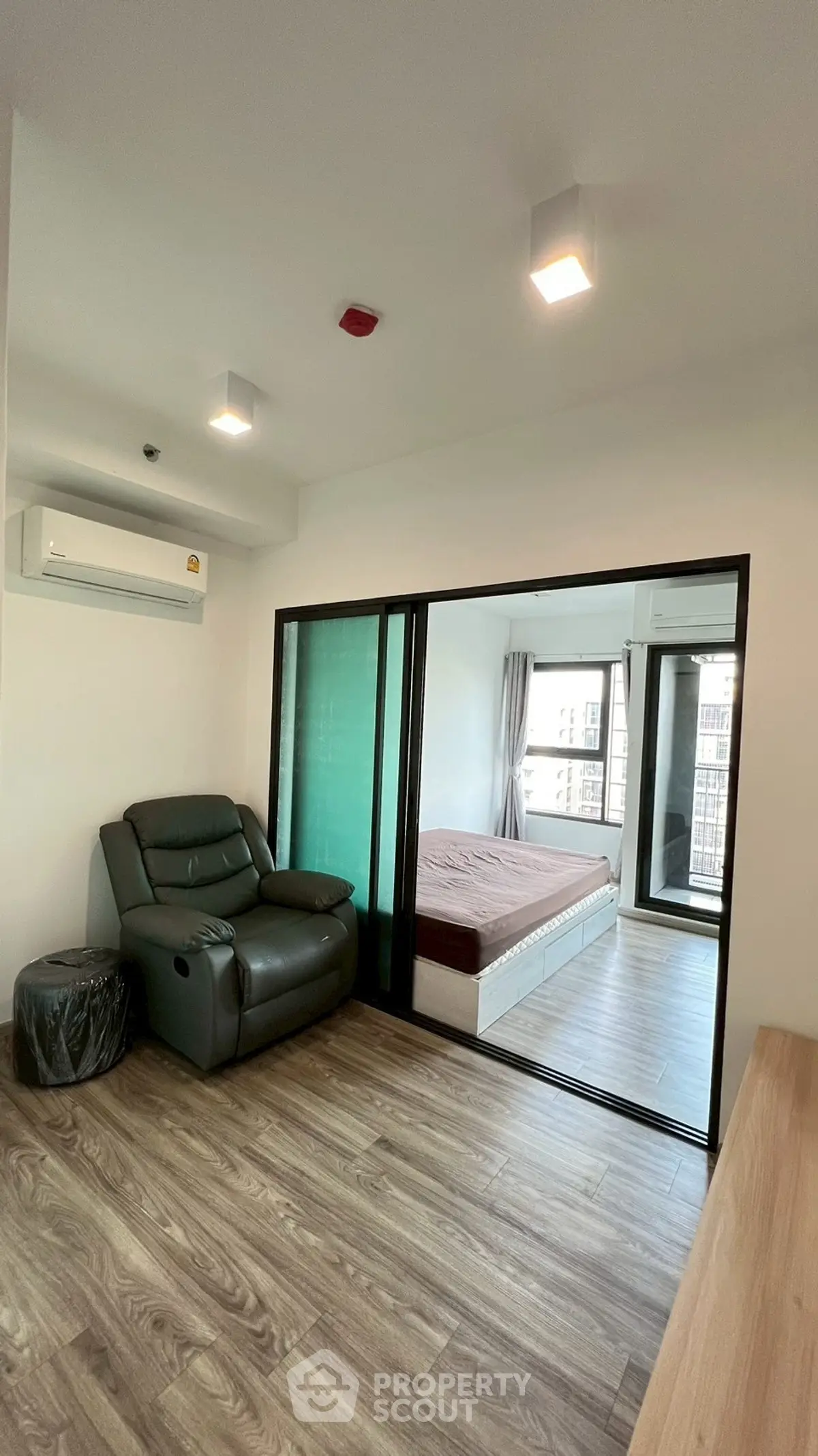 Modern apartment with sliding glass doors separating living area and bedroom, featuring sleek wood flooring.
