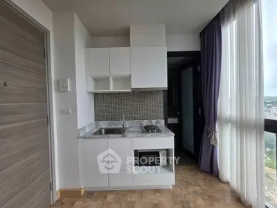Modern compact kitchen with large window and sleek cabinetry in a high-rise apartment.