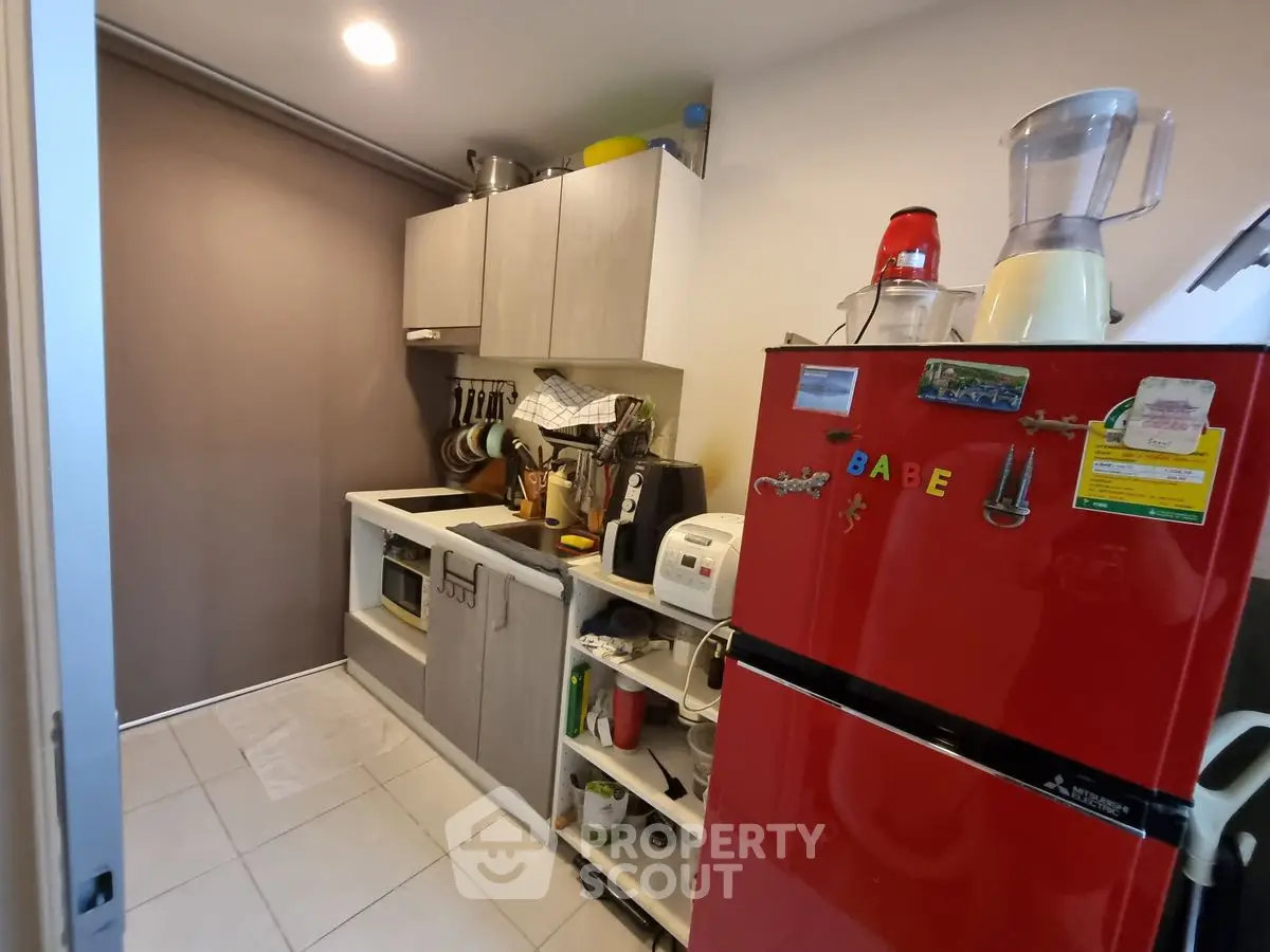 Compact kitchen with red fridge and modern cabinetry in cozy apartment.