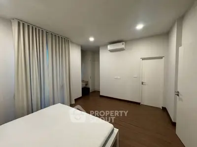 Spacious bedroom with modern design and wooden flooring, featuring air conditioning and elegant curtains.