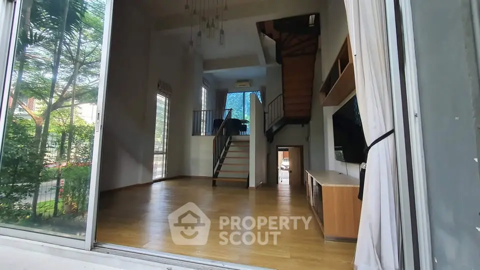 Spacious modern living room with high ceilings and large windows overlooking greenery.