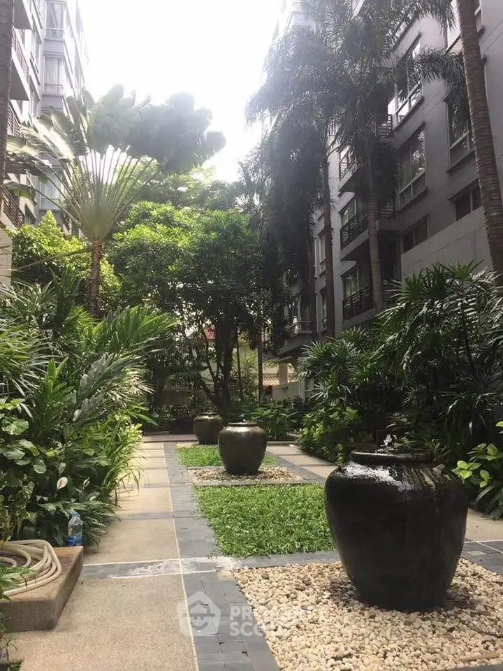 Lush garden courtyard in modern residential complex with tropical plants and decorative urns.
