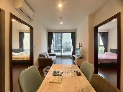 Modern apartment interior with open living area and two bedrooms, featuring large windows and stylish decor.