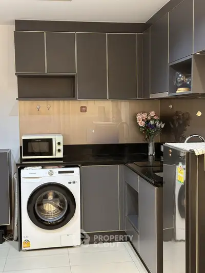 Modern kitchen with sleek cabinets, washing machine, and microwave in stylish apartment.