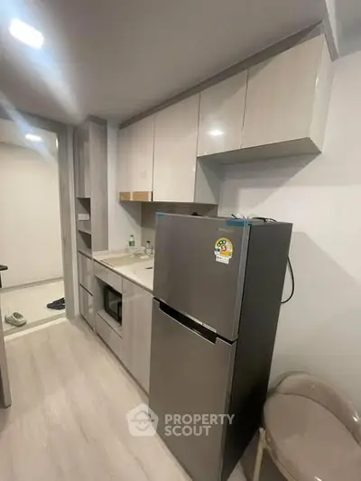 Modern kitchen with sleek cabinetry and stainless steel fridge in compact apartment.