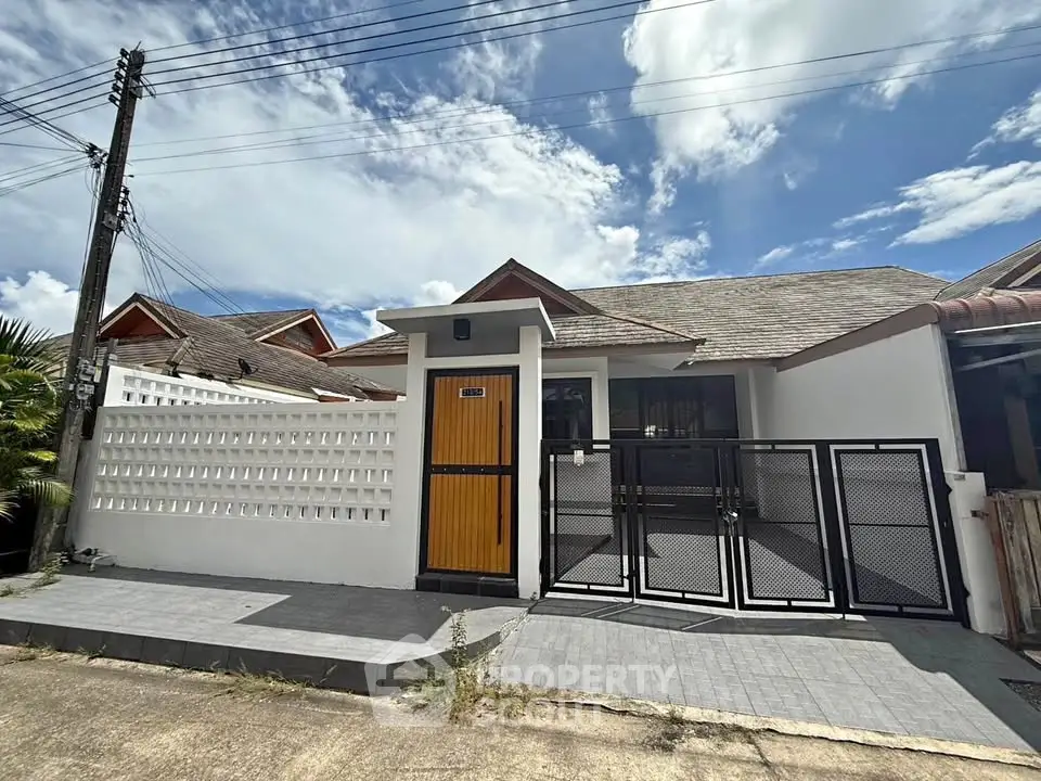 Charming single-story house with modern gate and vibrant yellow door under a clear blue sky.