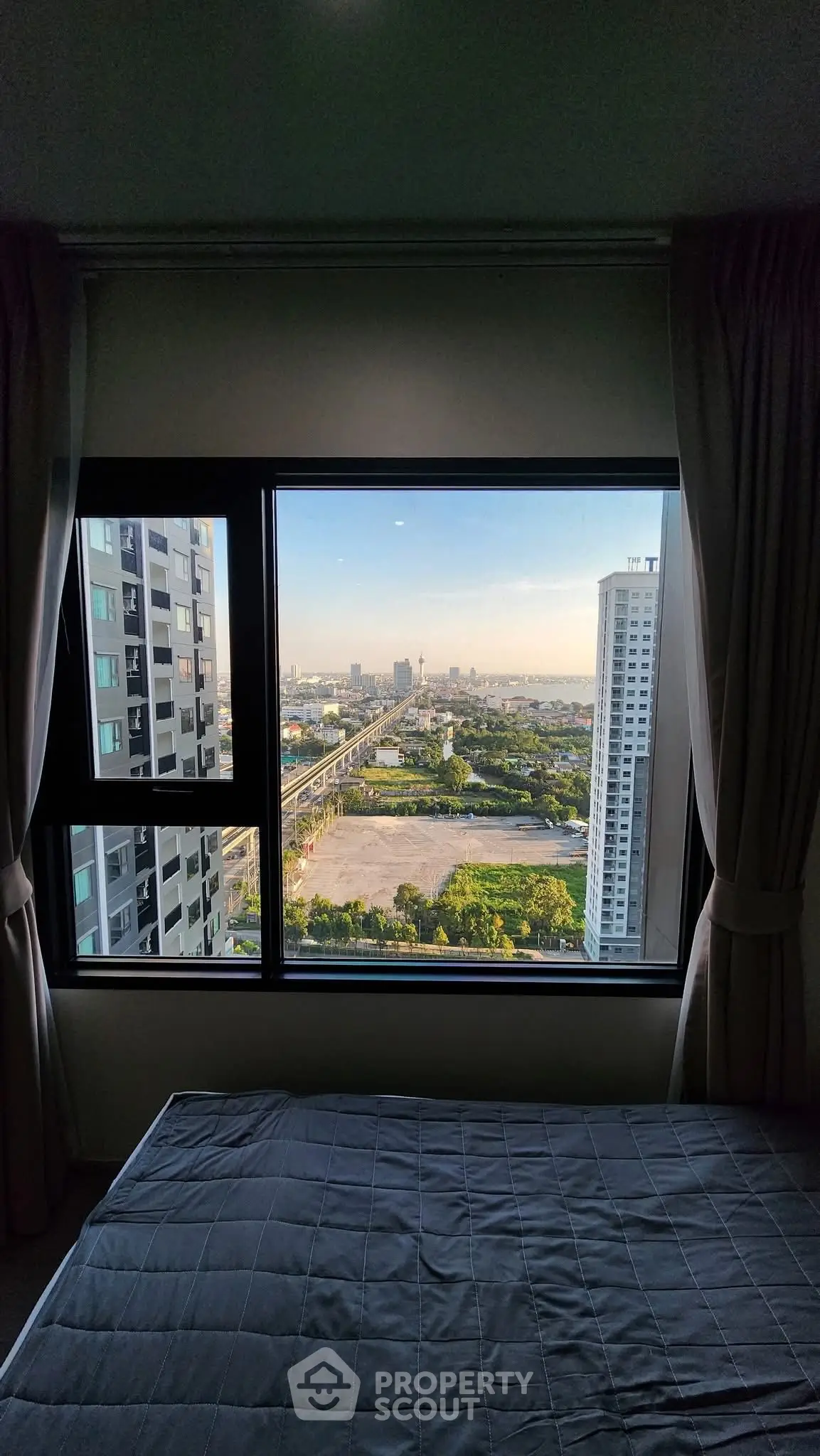 Stunning city view from a modern bedroom window, showcasing urban skyline and greenery.