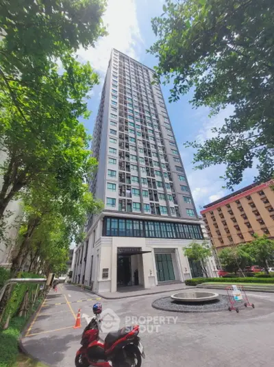 Modern high-rise building with lush greenery and clear blue sky, ideal urban living.