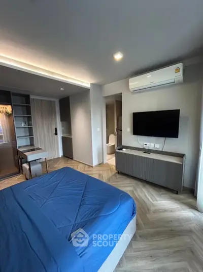 Modern bedroom with sleek design, featuring a blue bedspread, wall-mounted TV, and air conditioning.