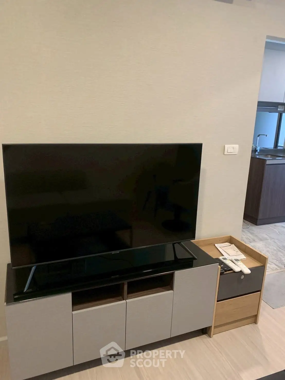 Modern living room with sleek TV stand and flat-screen TV, adjacent to a stylish kitchen area.