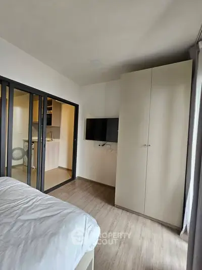 Modern bedroom with sliding doors and wall-mounted TV, adjacent to a compact kitchen.