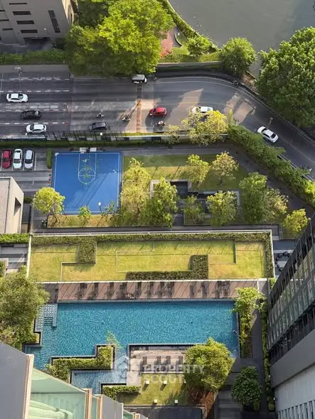 Stunning aerial view of luxury condominium with pool, garden, and sports court near a river.