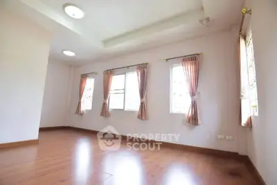 Spacious empty room with wooden flooring and large windows, perfect for customization.