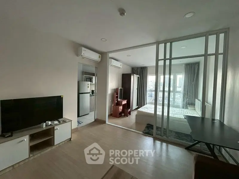 Modern apartment with open living room and bedroom, featuring glass partition and sleek furnishings.