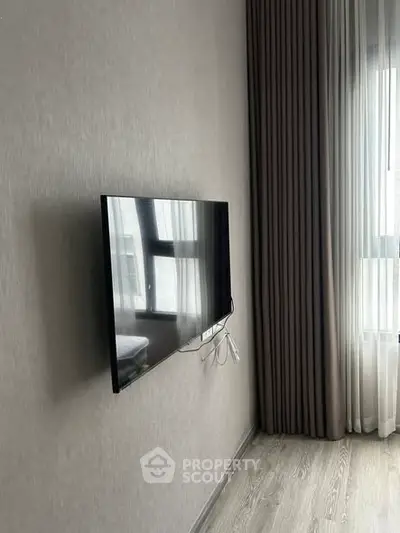 Modern living room with wall-mounted TV and large window with elegant curtains.