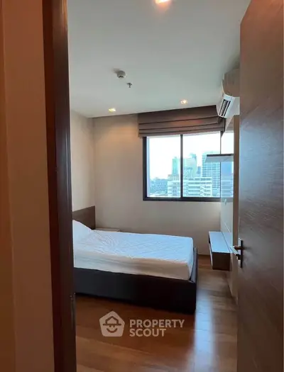 Cozy bedroom with city view, wooden flooring, and modern air conditioning unit.