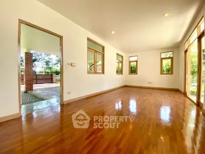 Spacious living room with wooden flooring and large windows offering natural light and garden view.