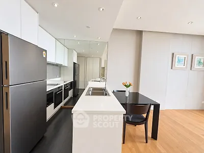 Modern kitchen with sleek black appliances and dining area in open layout apartment.