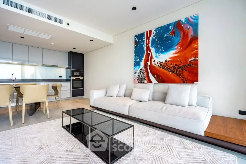 Modern living room with open kitchen, featuring stylish furniture and vibrant wall art.