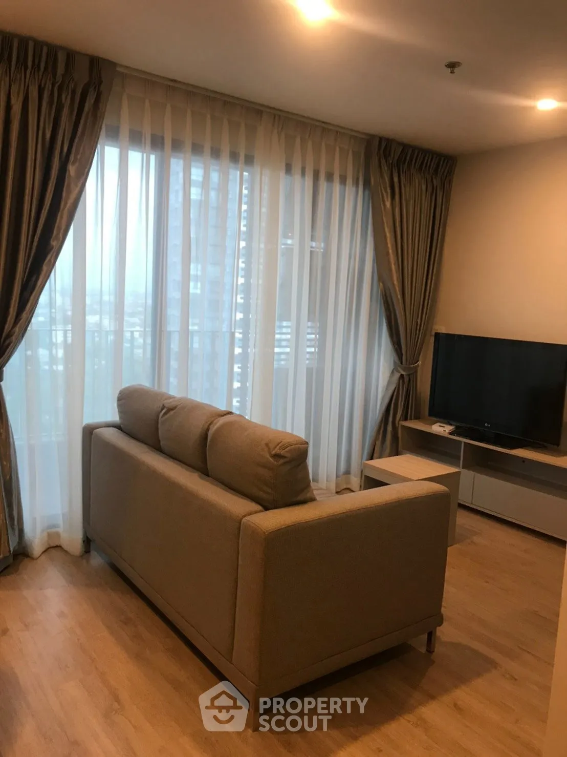Cozy living room with modern sofa and TV, featuring floor-to-ceiling windows and elegant curtains.