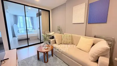 Modern living room with cozy sofa and stylish decor adjacent to a bright bedroom with glass sliding doors.