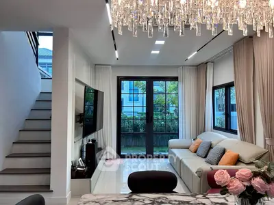 Luxurious living room with elegant chandelier and modern decor, featuring large windows and a cozy seating area.