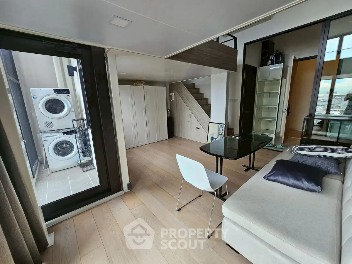 Modern living room with sleek design and laundry area, featuring a glass table and cozy seating.