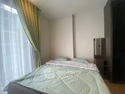 Cozy bedroom with soft green bedding and natural light from large window.