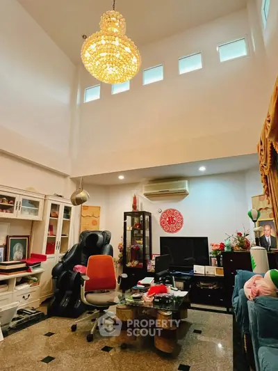 Spacious living room with high ceiling and elegant chandelier, featuring modern furniture and decor.