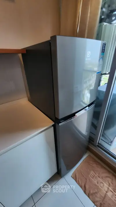 Modern kitchen with sleek stainless steel refrigerator and natural light from large window.