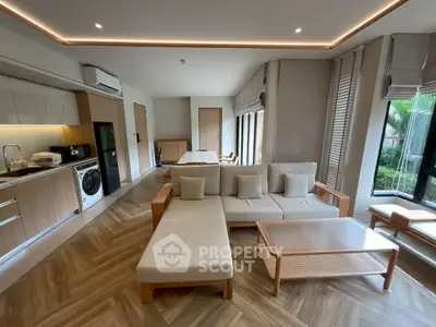 Modern living room with open kitchen, featuring stylish furniture and natural light.
