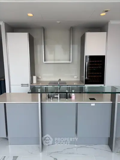 Modern kitchen with sleek cabinetry and built-in appliances, featuring a stylish glass countertop and marble flooring.