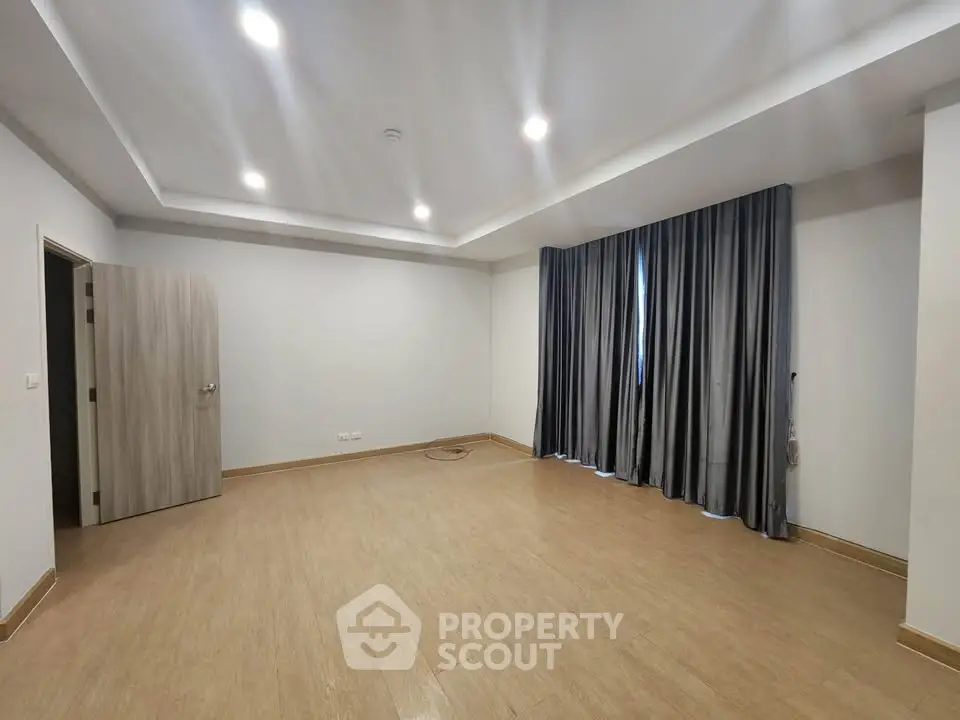 Spacious empty room with wooden flooring and elegant curtains