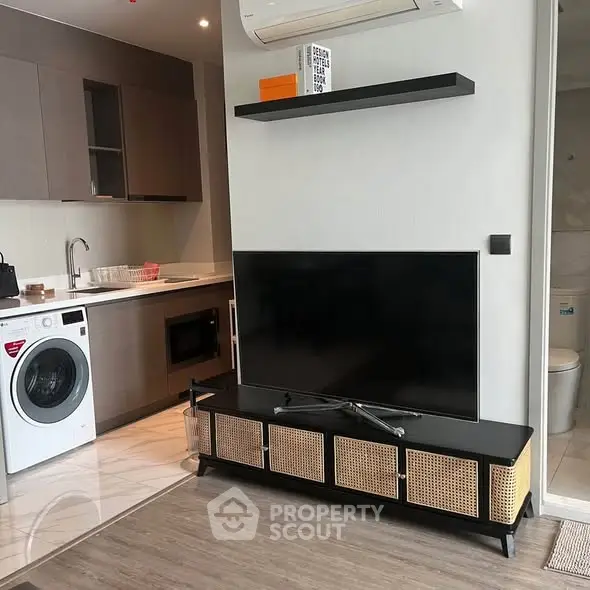 Modern apartment interior with sleek kitchen and cozy living area featuring a flat-screen TV and washing machine.