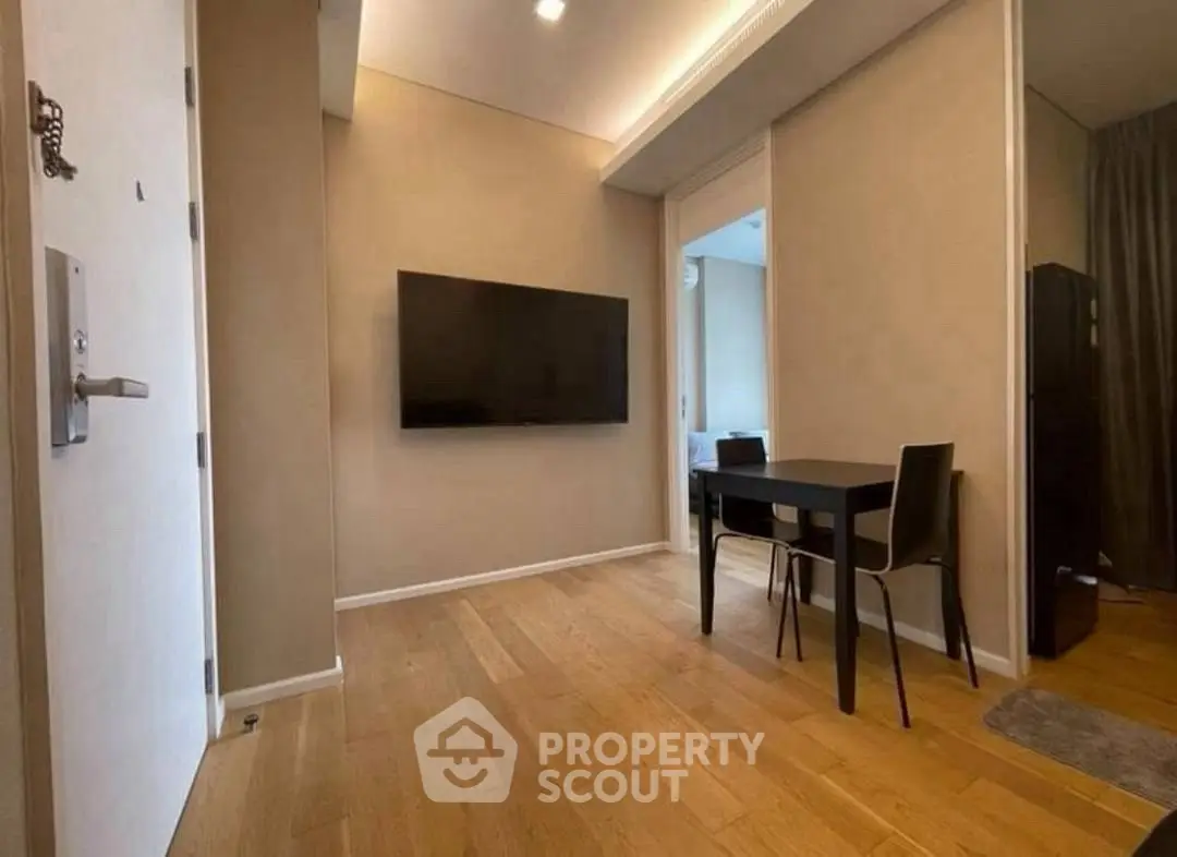 Modern apartment interior with wall-mounted TV and dining area, featuring wooden flooring and neutral tones.