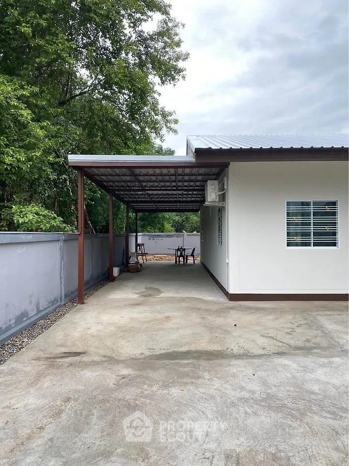 Charming single-story home with covered patio and spacious driveway, surrounded by lush greenery.