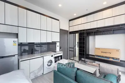 Modern studio apartment with sleek kitchen and cozy living area featuring a washing machine and smart TV.