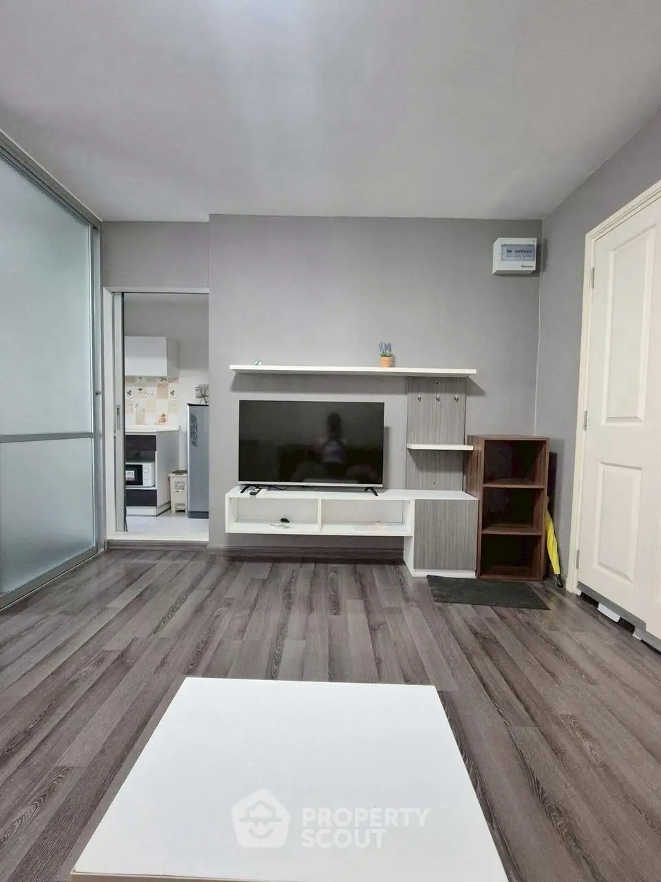Modern living room with sleek flooring and TV setup, adjacent to a stylish kitchen.