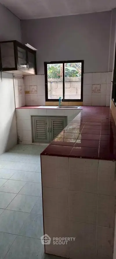 Cozy kitchen with red-tiled countertops and natural light from window.