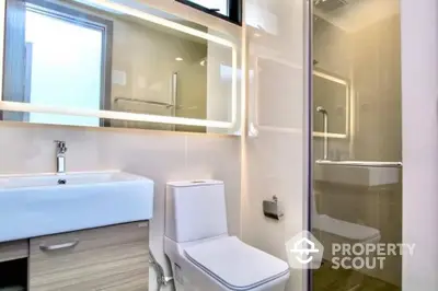 Modern bathroom with sleek design, featuring a large mirror, white fixtures, and a glass shower enclosure for a minimalist aesthetic.