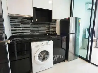 Modern kitchen with sleek black cabinetry, washing machine, and stainless steel fridge.
