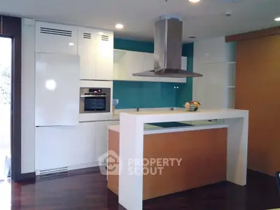 Modern kitchen with sleek white cabinets and built-in oven, featuring a stylish island and hardwood floors.